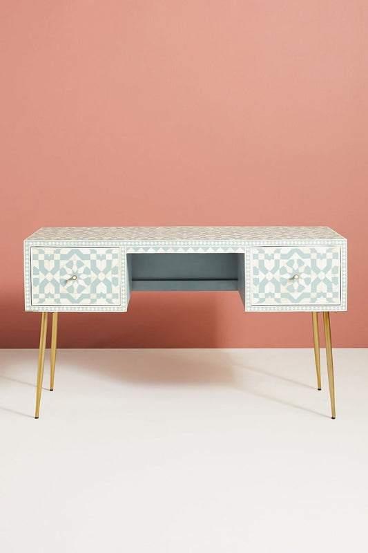 Top-down angle of a teal and white Moroccan bone inlay desk with two drawers and tapered gold metal legs against a peach and white wall.